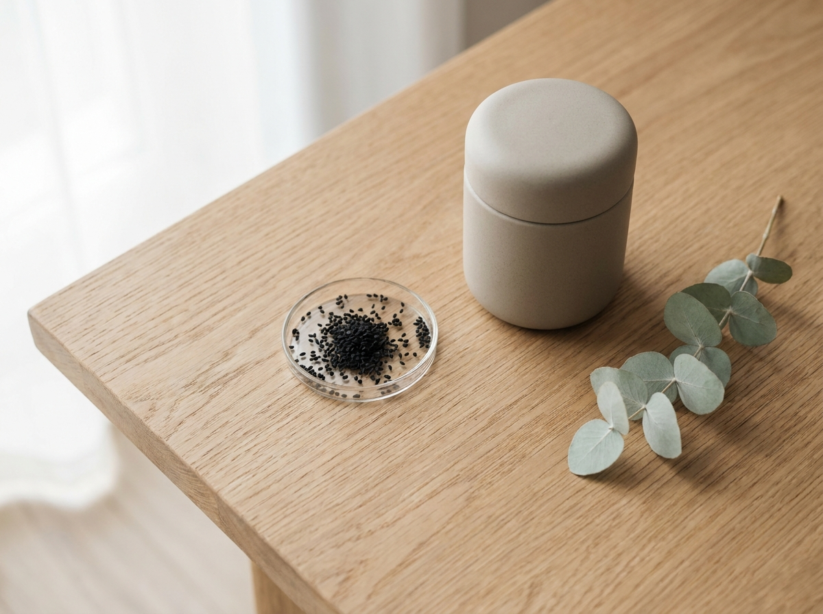 Flat lay minimaliste : jarre de soin en céramique, graines de nigelle et brin de sauge sur bois clair